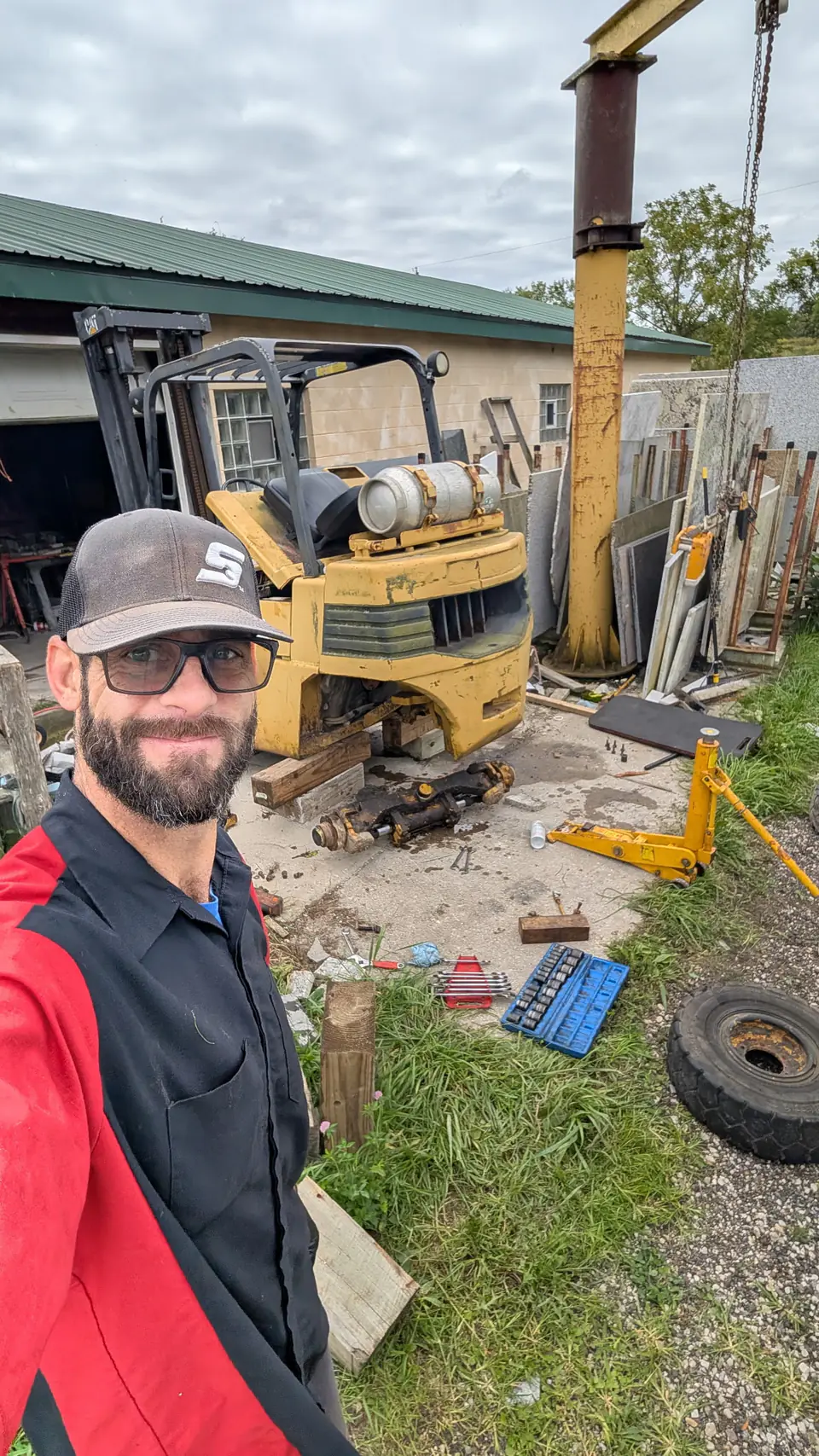 Technician beside a yellow forklift with its axle removed and tools laid out nearby