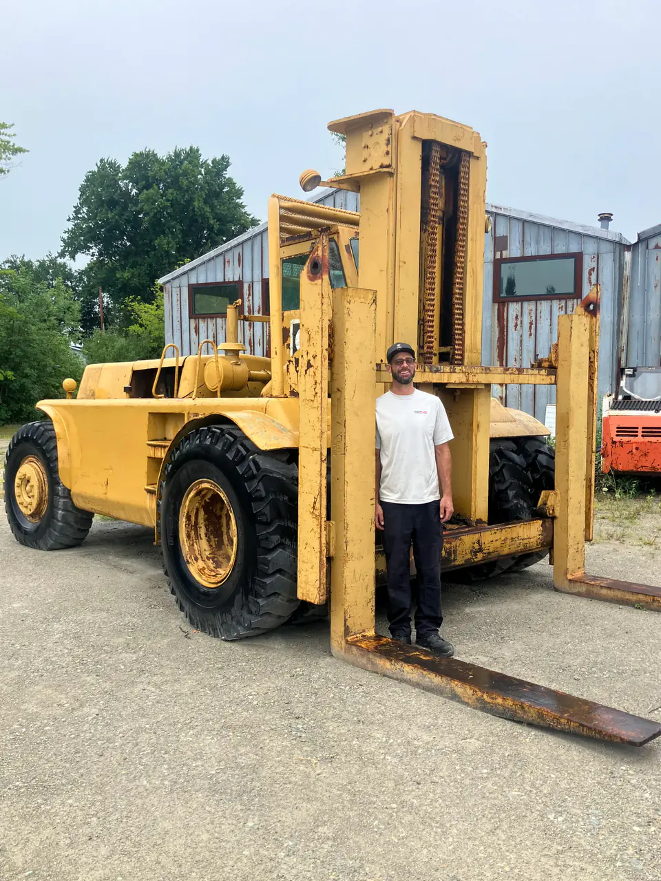 Technician standing beside the mast of a large yellow forklift outdoors