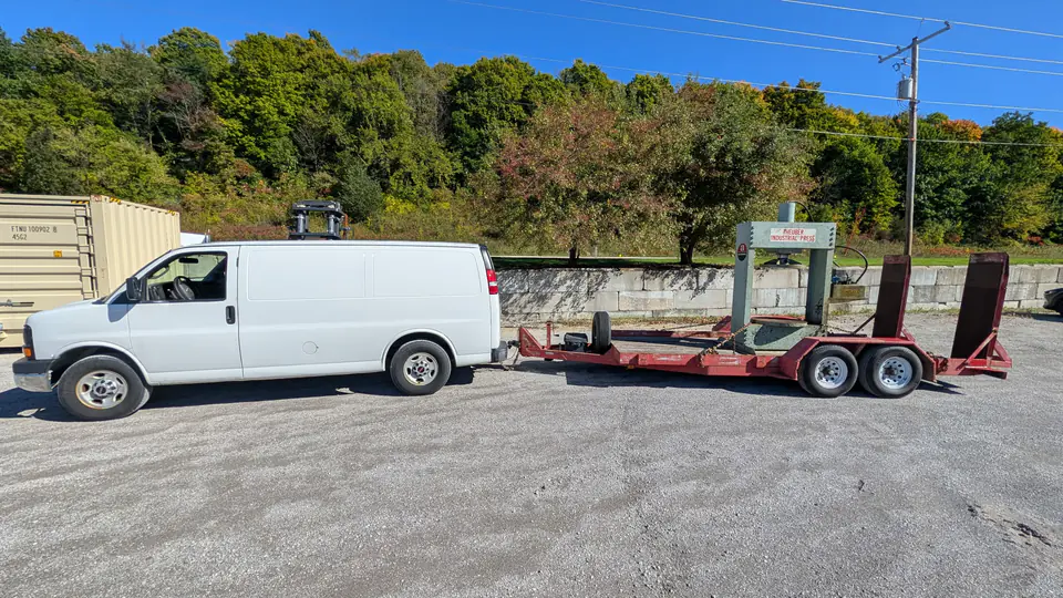 White service van beside an equipment trailer carrying an industrial press